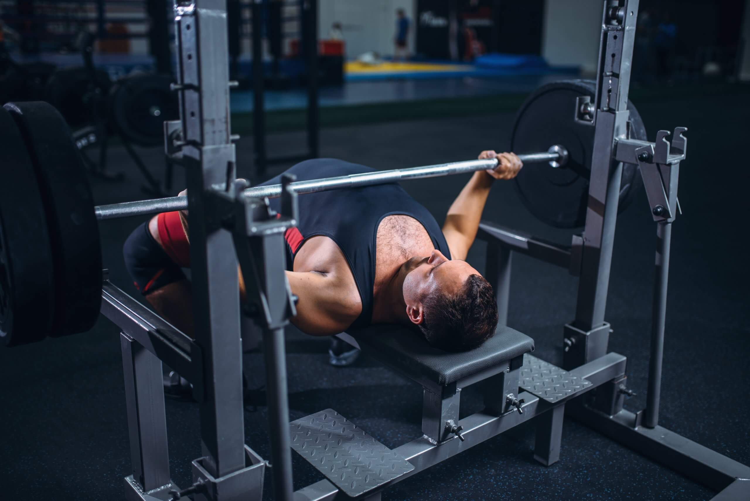 A weightlifter using an exercise machine with a barbell in a gym setting, demonstrating strength and focus.