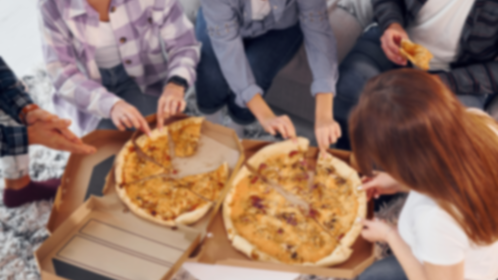 Group of people sitting around eating pizza with a blurred effect, representing social indulgence and flexible dieting.