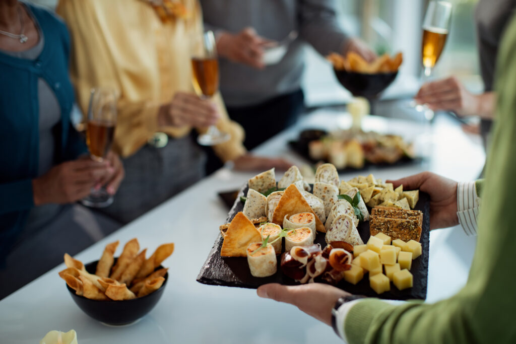 Businessman bringing food to an office party with coworkers gathered around.